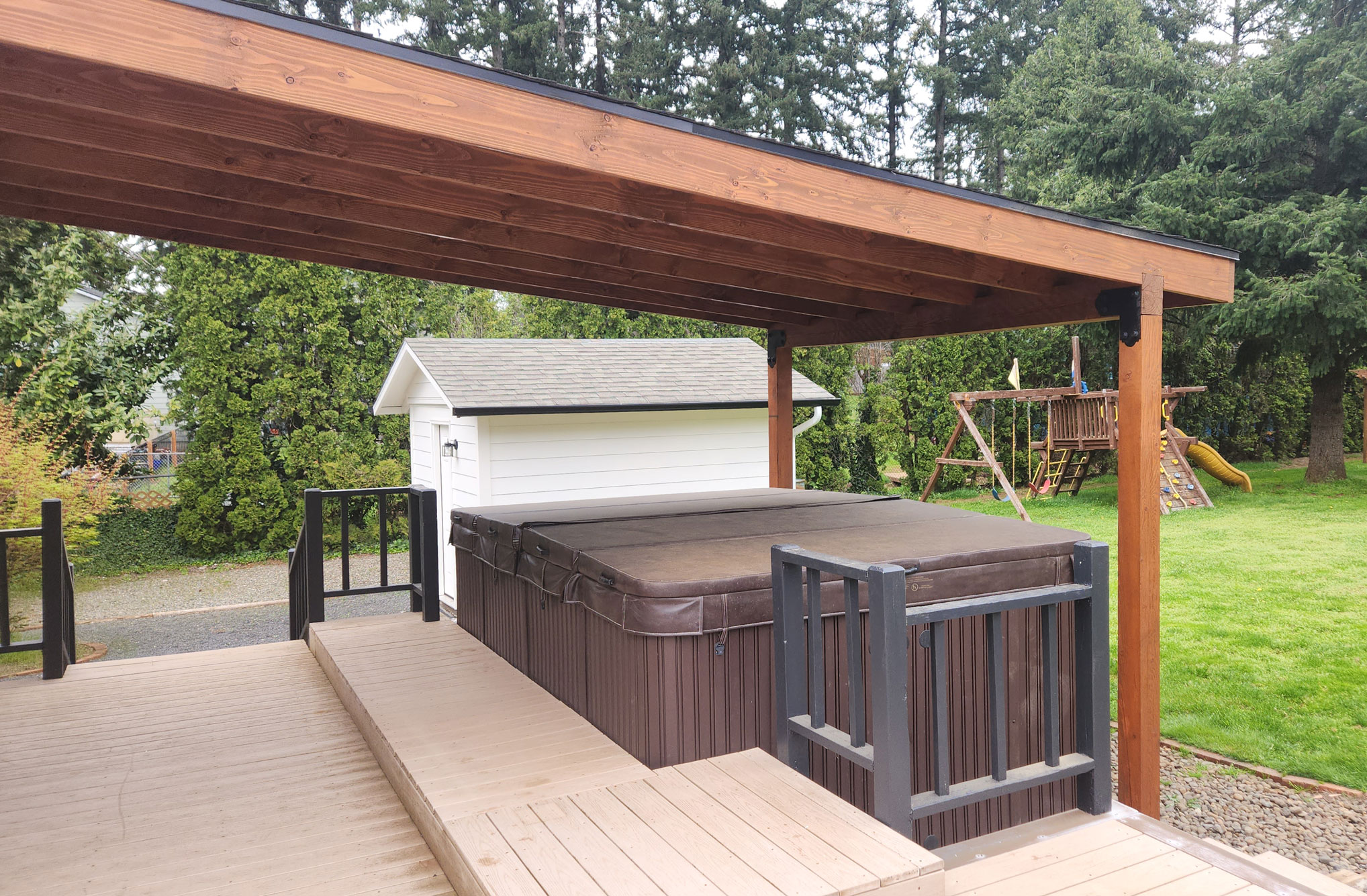 Porch roof built by Casa Bella Construction over porch and hot tub with backyard in background